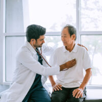 A doctor listening to an older man's heart.